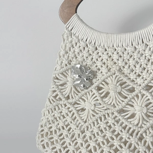 Détail d'un sac en macramé blanc avec des motifs de fleurs et une poignée en bois