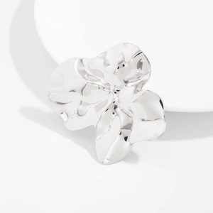 Détail d'une broche fleur argentée avec texture ondulée irrégulière sur support blanc