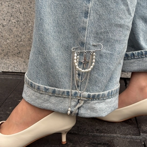 Detail of vintage style tassel brooch with pearls and chain on light blue denim jeans