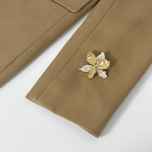 Détail d'une broche fleur irrégulière à texture métallique plissée sur un blazer camel