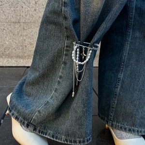 Dettaglio di spilla gotica con catene di perle e croce su un pantalone in denim blu