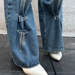 Dettaglio di spille da balia punk con ciondoli a cuore croce e nappe sui jeans