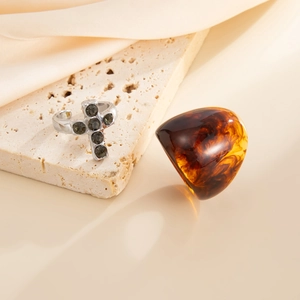 Macro detail of a silver cross ring with dark stones and an amber resin dome ring on stone