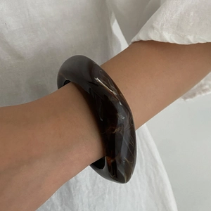 Close-up of a thick amber resin bangle featuring dark marble textures on a model wrist