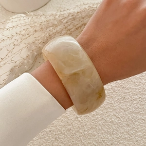 Detailansicht eines breiten Acryl-Armreifs mit bernsteinfarbener Marmorierung am Handgelenk