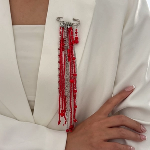 Detail of red beaded fringe brooch with silver chains on a white blazer lapel