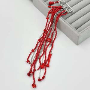Detailed close-up of handmade red bead tassel brooch with silver chains and beads