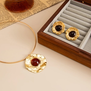Macro view of gold pendant and earrings with red resin stones on vintage newspaper