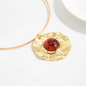 Detailed close-up of golden hammered metal pendant with translucent amber-red resin stone