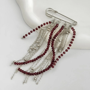 Detail of silver safety pin brooch featuring layered burgundy bead fringe and tassel chains