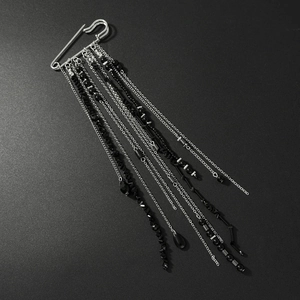 Detail view of silver tassel brooch with black beads and chains on dark background