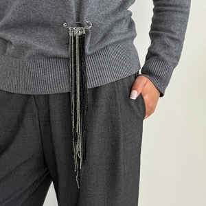 Close-up of a silver safety pin brooch with long black and silver beaded tassel chains