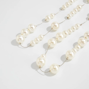 Detail van lange parelketting met gegradueerde kralen en een fijne metalen ketting