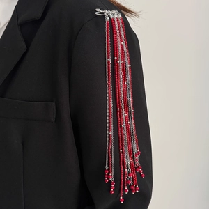 Detail view of red crystal bead tassels and silver chains on a black suit blazer shoulder