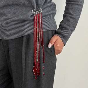 Detail view of a long red crystal beaded tassel brooch with silver chain on a grey blazer