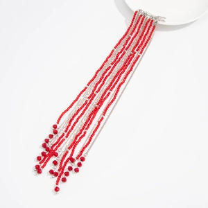 Detail of red beaded tassel brooch with silver metal chains on a white ceramic plate