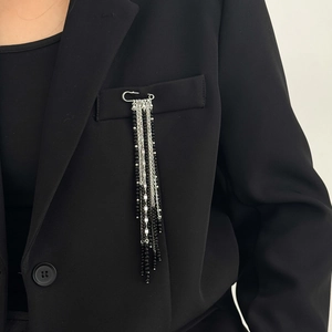 Detail of beaded tassel brooch with silver chains and black crystals on a blazer