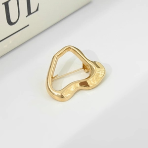 Close-up of golden liquid lava metal brooch in irregular heart shape with artistic hollow design