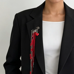Detail of silver safety pin brooch with red beaded fringe and heart pendant on black suit