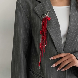 Detail of red beaded tassel brooch with heart pendant on a grey pinstripe suit