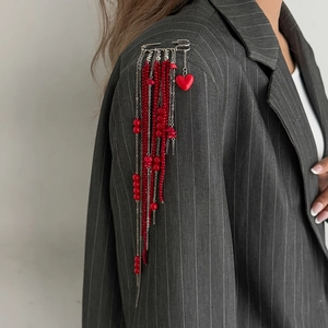 Detail view of red beaded fringe brooch with heart charm on a gray striped suit jacket