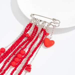 Macro detail of silver safety pin brooch with red beads, fringe chains, and heart pendant
