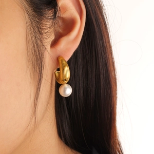 Close-up of gold C-shape drop earrings with textured metal and elegant white pearls