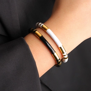 Close-up of stacked colorful striped enamel cuff bracelets in gold, black, and white