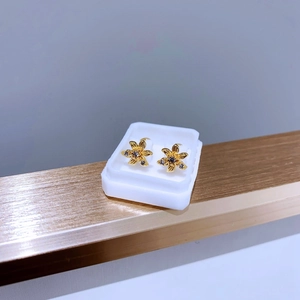 Detailaufnahme goldener Blumenohrringe mit dunklen Zirkonsteinen und gebürsteter Textur