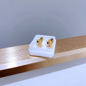 Makroaufnahme goldener Schmetterlings- und Bienenohrringe mit Zirkonia auf weißem Ständer