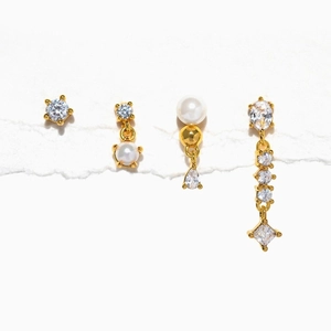 Detail von vierteiligem Set aus goldfarbenen Zirkon- und Perlenohrringen auf Weiß