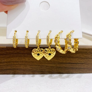 Detail of three-pair gold earring set featuring micro-pave zircons and evil eye heart charms