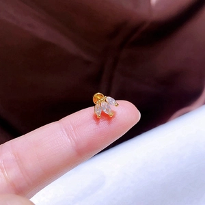 Makroaufnahme von winzigem Gold-Kleeblatt-Ohrstecker mit Zirkonia auf einer Fingerspitze