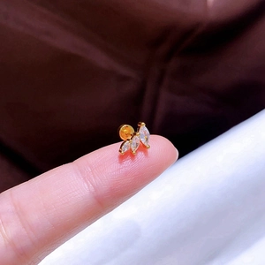 Nahaufnahme eines goldfarbenen Piercings mit drei Zirkonia-Steinen auf einer Fingerspitze