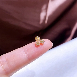Detailansicht eines goldenen Kleeblatt-Ohrrings mit Zirkonia auf einer Fingerspitze