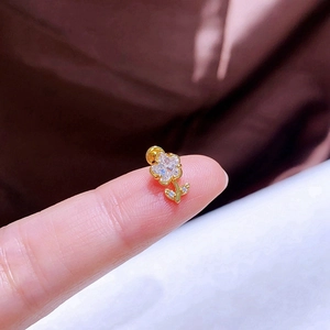 Makroaufnahme eines kleinen Goldohrrings mit Zirkonia-Klee auf einer Fingerspitze als Referenz