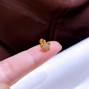 Makroaufnahme eines winzigen goldenen Schildkröten-Ohrrings mit Zirkonia auf der Fingerspitze