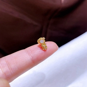 Makroaufnahme eines kleinen goldfarbenen Ohrsteckers mit Zirkon auf einer Fingerspitze