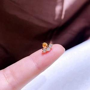 Nahaufnahme eines kleinen goldenen Bogens mit drei klaren Zirkonias auf einer Fingerspitze