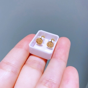 Nahaufnahme kleiner goldener Smiley-Ohrstecker in weißer Box mit Hand als Referenz