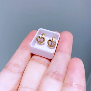Minimalistische goldene Herz-Ohrstecker in kleiner Größe auf den Fingerspitzen