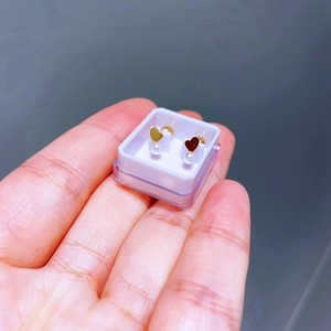 Detailansicht herzförmiger Perlenohrringe in einer transparenten Box in der Hand