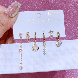 Parure de 6 boucles d'oreilles dorées avec zircons cœur et fleur sur fond rose