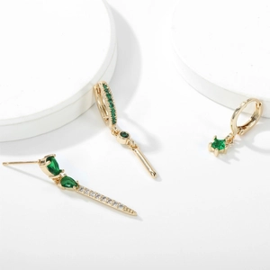 Detailed view of three-piece gold earring set with emerald green zircons on white stands