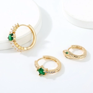 Macro shot of gold-plated hoop earrings set with green emerald stones and snake design