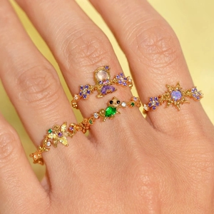 Detailansicht vergoldeter Ringe mit Schmetterling, Lilie und bunten Zirkonsteinen