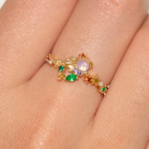 Detail eines vergoldeten Rings mit bunten Kristallen und irisierendem Hauptstein