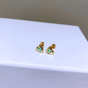 Makro-Detail goldener Herzohrringe mit grünem Edelstein und funkelnden kleinen Diamanten