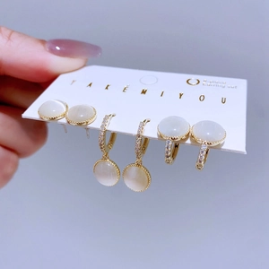Detail view of a 3-pair gold earring set featuring round cat eye stones and rhinestones