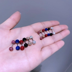 Nahaufnahme von Titanstahl-Hantel-Ohrringen mit bunten Glitzerkugeln in der Hand